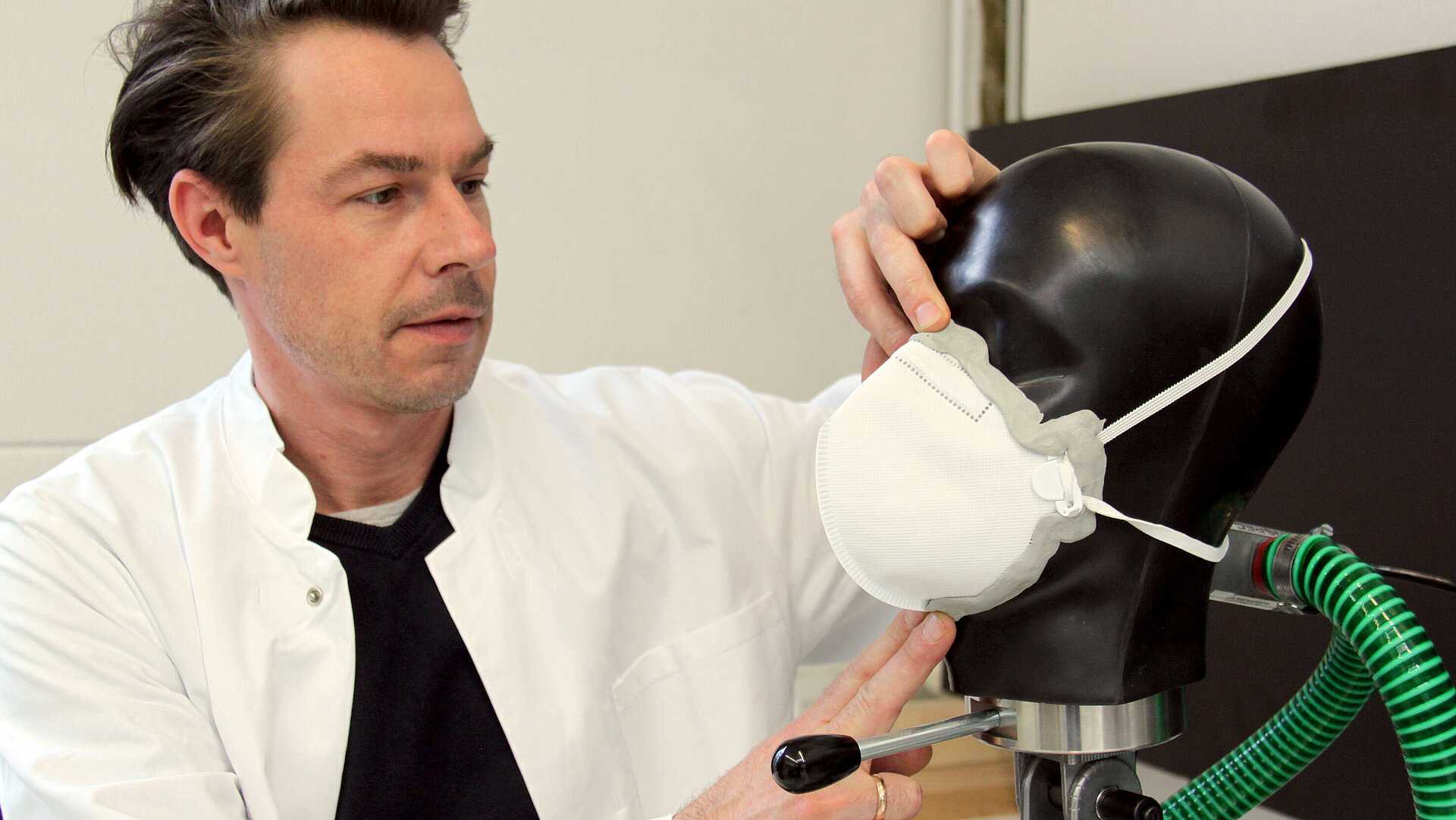 Ein Prüfer in einem Laborkittel prüft eine Atemschutzmaske an einem Prüfkopf