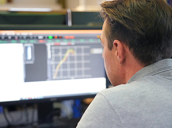 View over the shoulder of a test engineer looking at a monitor. Test diagrams can be seen on the monitor